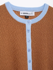 Nahaufnahme der braunen Strickjacke mit hellblauem Rippsaum und runden Knöpfen