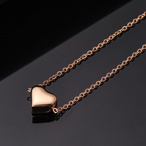 Close-up of rose gold heart pendant on a thin chain over a black reflective surface