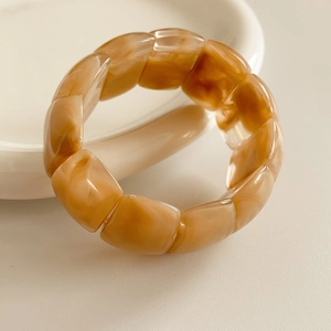 Detail of amber marble texture acrylic geometric beaded stretch bracelet on a white plate