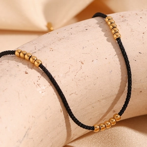 Detail of 18K gold-plated steel beads on a black woven anklet over a textured cylinder