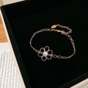 Detail of a gold flower bracelet with a pearl center displayed in a black velvet box