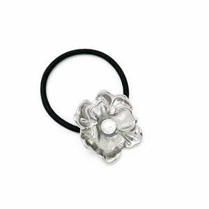 Detailed view of black elastic hair tie with silver flower charm and central pearl