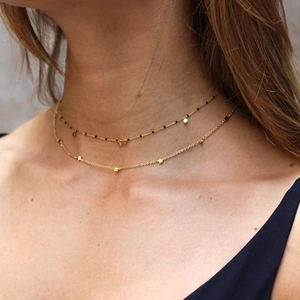 Detail of layered gold star necklace with black beads and circular sequins on model