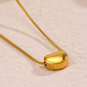 Elegant gold bean pendant necklace with minimalist thin chain on a textured surface