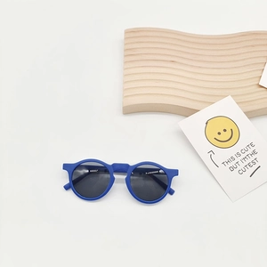 Close-up of matte dark blue round kids sunglasses on a minimalist white backdrop