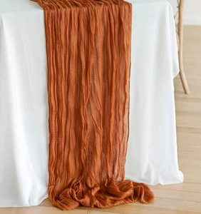 Close-up detail of terracotta wrinkled cheesecloth table runner with soft natural texture