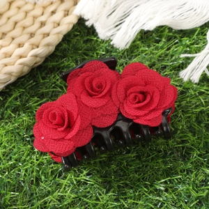Close-up of elegant black hair claw clip with three red velvet roses on green grass