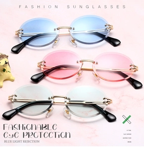 Flat lay of rimless oval sunglasses in blue pink and grey colors with gold metal frames