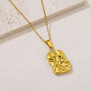 Detail of gold rectangular pendant with wrinkled texture on a beige marble surface