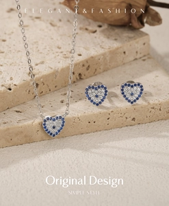 Detail of silver heart-shaped necklace and stud earrings set with blue crystal evil eye