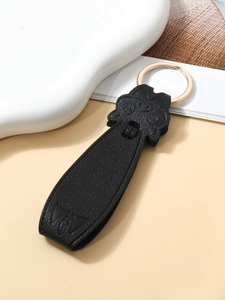 Close-up of black PU leather pig keychain with golden metal ring on textured background