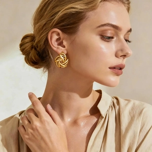 Close-up of golden geometric woven knot stud earrings worn by a model in soft lighting