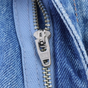 Macro shot of high-quality SAB metal zipper and blue denim fabric texture on women's jeans