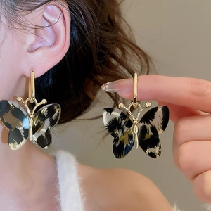 Detailed macro view of gold-rimmed butterfly earrings with leopard print acetate pattern