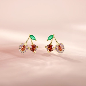 Close-up of golden cherry earrings with red stones and pink gemstone heart accents