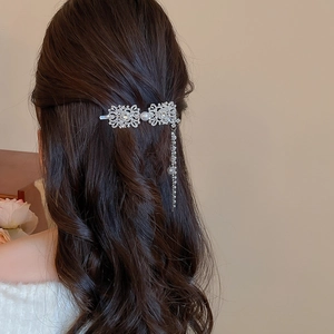 Detailed view of a silver tassel hair clip with rhinestones and pearls on wavy brown hair
