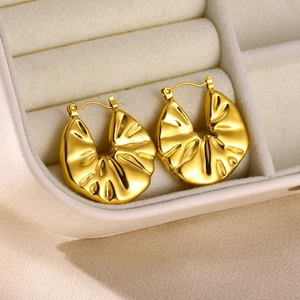 Detailed close-up of gold-plated hoop earrings with irregular hammered metal texture