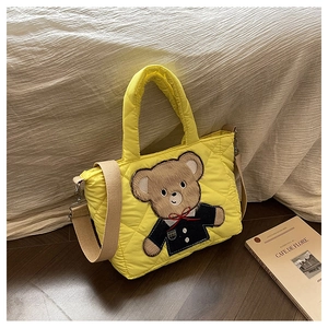 Detail of yellow quilted tote bag featuring a cute brown teddy bear embroidery and strap