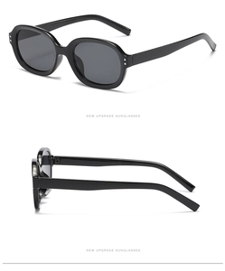 Detail view of black oval sunglasses featuring classic double rivet accents on the frame