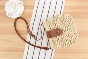 Detail view of woven paper rope bag with brown leather flap and slim shoulder strap