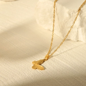 Detail of a golden butterfly pendant with radial textures on a twisted rope chain necklace