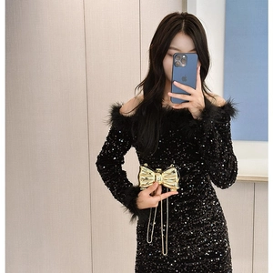 Elegant black sequin mini dress with feather trim and a gold bow-shaped clutch bag
