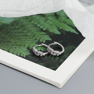 Detail of silver S925 pave earrings placed on an open book with green botanical patterns