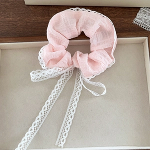 Detail of pink scrunchie with white lace trim and long ribbons on a tray