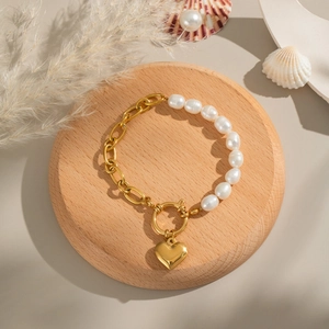 Elegantes Goldketten-Armband mit weißen Perlen und Herzanhänger auf Holzsockel