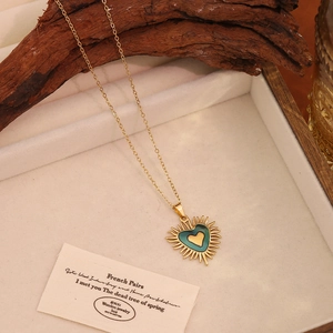 Gros plan du pendentif cœur doré avec émail sarcelle sur un plateau à bijoux en bois