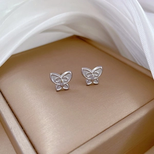 Macro shot of silver butterfly stud earrings on golden display with white silk cloth