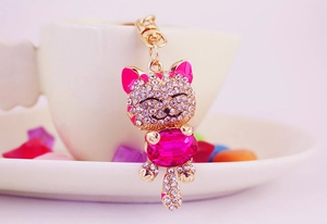 Detail of fortune cat keychain with pink crystal and rhinestones on a porcelain plate