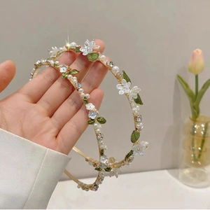 Elegant floral headband with white pearls and green leaves on a gold frame
