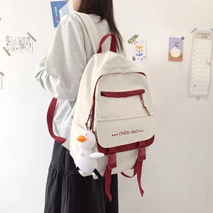 Detail of white school backpack with burgundy straps and cute plush duck pendant