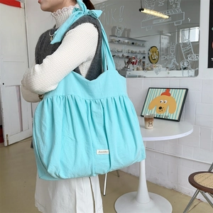 Detailansicht der hellblauen gefalteten Canvas-Tasche, getragen von einem Modell im Cafe