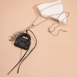 Détail d'un long collier en acier avec pendentif sac en strass noirs et pompon cuir
