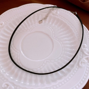 Detail view of a minimalist black choker necklace on a white vintage ceramic plate