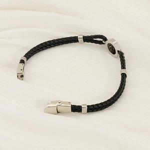 Detail of black braided leather bracelet with stainless steel magnetic clasp on white silk