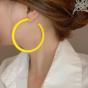 Close-up of a large matte yellow hoop earring worn by a model in a minimal style