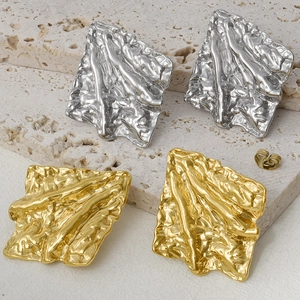Detailed close-up of 18k gold and silver irregular crinkle earrings on a stone texture