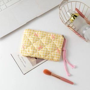 Detailed shot of yellow quilted floral cosmetic bag with pink bow pattern and zipper