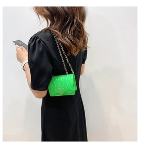 Close-up of vibrant green mini crossbody bag with gold chain strap on a black dress