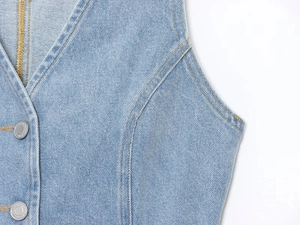 Détail de gilet en jean à col en V avec surpiqûres jaunes et boutons métalliques