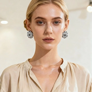 Detail view of a model wearing silver metallic woven knot stud earrings in a bright setting