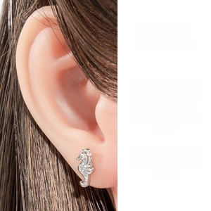 Detailed close-up of a zircon-inlaid seahorse cartilage earring on ear and white background