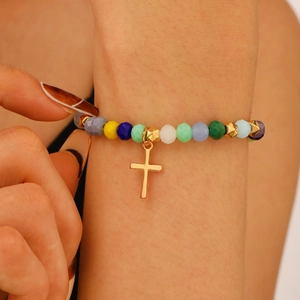 Close-up of a colorful beaded bracelet with a polished gold cross pendant on a model's wrist