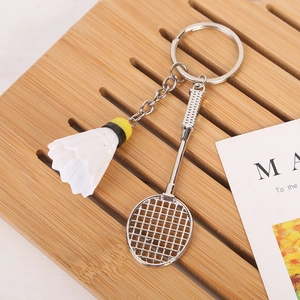 Macro shot of silver metal badminton racket and white shuttlecock keychain on a wooden tray