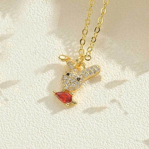 Macro detail of gold-tone necklace with sparkling white zircon rabbit and red heart stone