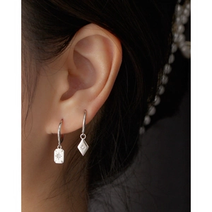 Close-up of geometric starburst rectangular and rhombic charms on silver hoop earrings