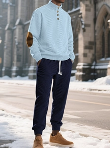 Detail of light blue cable knit sweater with brown elbow patches and buttoned collar